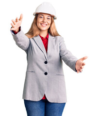 Canvas Print - Beautiful young woman wearing architect hardhat looking at the camera smiling with open arms for hug. cheerful expression embracing happiness.