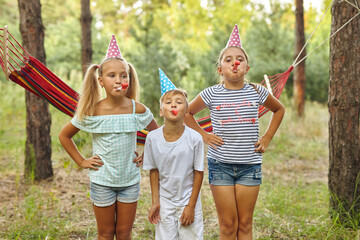 birthday, childhood and celebration concept - happy kids blowing party horns and having fun in summer outdoors