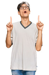 Canvas Print - Young hispanic man wearing casual clothes and glasses amazed and surprised looking up and pointing with fingers and raised arms.