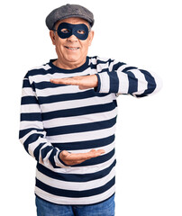 Wall Mural - Senior handsome man wearing burglar mask and t-shirt gesturing with hands showing big and large size sign, measure symbol. smiling looking at the camera. measuring concept.