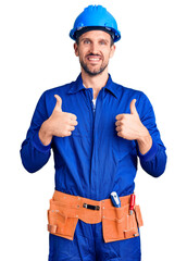 Canvas Print - Young handsome man wearing worker uniform and hardhat success sign doing positive gesture with hand, thumbs up smiling and happy. cheerful expression and winner gesture.