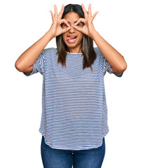 Sticker - Young latin girl wearing casual clothes doing ok gesture like binoculars sticking tongue out, eyes looking through fingers. crazy expression.