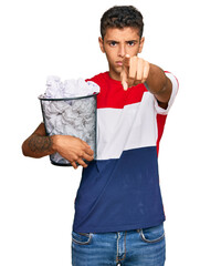 Canvas Print - Young handsome african american man holding paper bin full of crumpled papers pointing with finger to the camera and to you, confident gesture looking serious