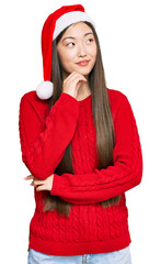 Poster - Young chinese woman wearing christmas hat with hand on chin thinking about question, pensive expression. smiling and thoughtful face. doubt concept.