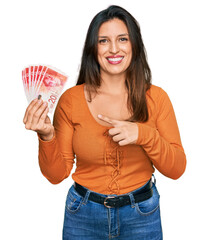 Sticker - Beautiful hispanic woman holding 20 israel shekels banknotes smiling happy pointing with hand and finger