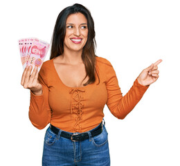 Wall Mural - Beautiful hispanic woman holding 100 yuan chinese banknotes smiling happy pointing with hand and finger to the side