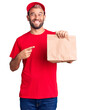 Young handsome blond man holding delivery paper bag smiling happy pointing with hand and finger