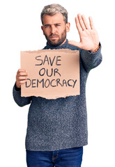 Poster - Young blond man holding save our democracy cardboard banner with open hand doing stop sign with serious and confident expression, defense gesture