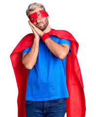 Wall Mural - Young blond man wearing super hero custome sleeping tired dreaming and posing with hands together while smiling with closed eyes.