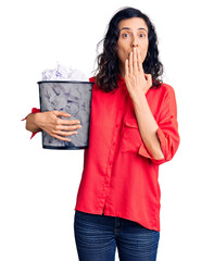 Wall Mural - Young beautiful hispanic woman holding paper bin full of crumpled papers covering mouth with hand, shocked and afraid for mistake. surprised expression