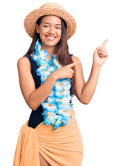 Canvas Print - Young beautiful latin girl wearing hawaiian lei and summer hat smiling and looking at the camera pointing with two hands and fingers to the side.