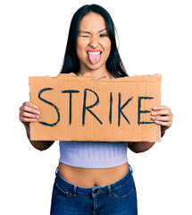 Wall Mural - Beautiful hispanic woman holding strike banner cardboard sticking tongue out happy with funny expression.