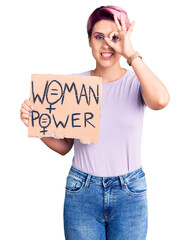 Canvas Print - Young beautiful woman with pink hair holding woman power banner smiling happy doing ok sign with hand on eye looking through fingers