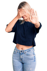 Wall Mural - Young beautiful blonde woman wearing casual t-shirt covering eyes with hands and doing stop gesture with sad and fear expression. embarrassed and negative concept.