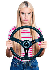 Wall Mural - Beautiful blonde woman holding steering wheel depressed and worry for distress, crying angry and afraid. sad expression.