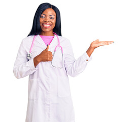 Canvas Print - Young african american woman wearing doctor stethoscope showing palm hand and doing ok gesture with thumbs up, smiling happy and cheerful