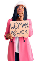 Poster - Young african american woman wearing architect helmet holding woman power banner serious face thinking about question with hand on chin, thoughtful about confusing idea