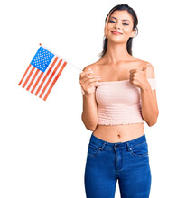 Young Beautiful Woman Holding United States Flag Smiling Happy And Positive, Thumb Up Doing Excellent And Approval Sign