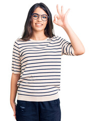 Wall Mural - Brunette teenager girl wearing casual clothes and glasses smiling positive doing ok sign with hand and fingers. successful expression.