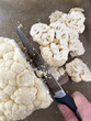 close up of a hand cutting cauliflower with a knife
