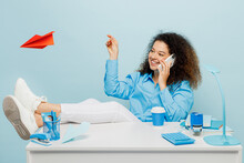 Young Fun Employee Business Woman Wear Casual Shirt Work Sit On White Office Desk Talk Speak On Mobile Cell Phone Play With Paper Plane Isolated On Plain Pastel Light Blue Background Studio Portrait.