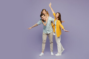 Wall Mural - Full body young parents mom dad with child kid daughter girl 6 years old wear blue yellow casual clothes giving piggyback ride to joyful, sit on back spread hands isolated on plain purple background.