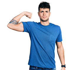 Wall Mural - Young hispanic man wearing casual t shirt strong person showing arm muscle, confident and proud of power