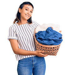 Sticker - Young woman holding laundry basket looking positive and happy standing and smiling with a confident smile showing teeth