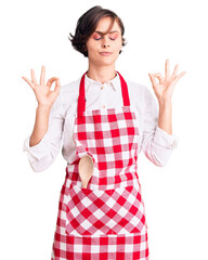 Poster - Beautiful young woman with short hair wearing professional cook apron relax and smiling with eyes closed doing meditation gesture with fingers. yoga concept.