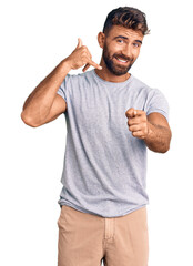 Wall Mural - Young hispanic man wearing casual clothes smiling doing talking on the telephone gesture and pointing to you. call me.