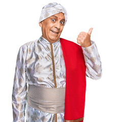 Poster - Senior hispanic man wearing tradition sherwani saree clothes smiling with happy face looking and pointing to the side with thumb up.