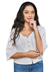 Wall Mural - Brunette young woman wearing casual clothes looking confident at the camera with smile with crossed arms and hand raised on chin. thinking positive.