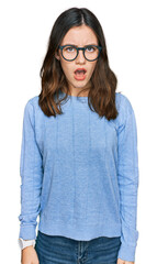 Young beautiful woman wearing casual clothes and glasses in shock face, looking skeptical and sarcastic, surprised with open mouth