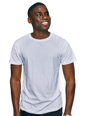 Wall Mural - Young african american man wearing casual white t shirt looking away to side with smile on face, natural expression. laughing confident.