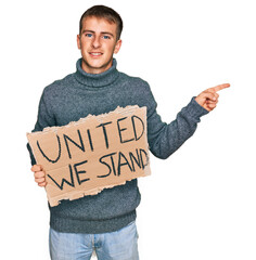 Sticker - Young blond man holding united we stand banner smiling happy pointing with hand and finger to the side