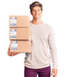 © Krakenimages.com - Young handsome man holding delivery package looking positive and happy standing and smiling with a confident smile showing teeth
