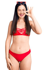 Poster - Young beautiful caucasian woman wearing bikini smiling positive doing ok sign with hand and fingers. successful expression.