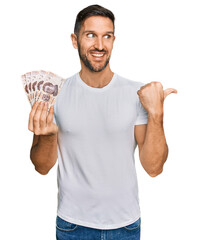 Sticker - Handsome man with beard holding 50 mexican pesos banknotes pointing thumb up to the side smiling happy with open mouth