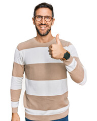 Canvas Print - Handsome man with beard wearing casual clothes and glasses doing happy thumbs up gesture with hand. approving expression looking at the camera showing success.