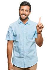 Wall Mural - Handsome hispanic man wearing casual clothes showing and pointing up with finger number one while smiling confident and happy.