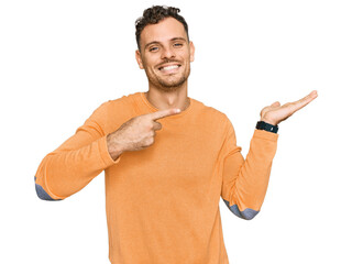 Canvas Print - Young hispanic man wearing casual clothes amazed and smiling to the camera while presenting with hand and pointing with finger.