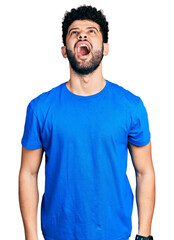 Canvas Print - Young arab man with beard wearing casual blue t shirt angry and mad screaming frustrated and furious, shouting with anger. rage and aggressive concept.