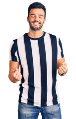 Wall Mural - Young handsome hispanic man wearing striped tshirt very happy and excited doing winner gesture with arms raised, smiling and screaming for success. celebration concept.