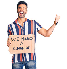 Wall Mural - Young handsome hispanic man holding we need a change banner screaming proud, celebrating victory and success very excited with raised arms