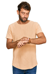 Poster - Handsome young man with beard wearing casual tshirt checking the time on wrist watch, relaxed and confident