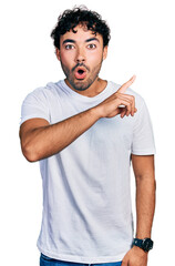 Canvas Print - Hispanic young man with beard wearing casual white t shirt surprised pointing with finger to the side, open mouth amazed expression.