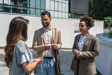 Wall Mural - Group of business people walk outside in front of office buildings. Businessman and two businesswomen sharing experience ideas and tactic for successful strategy and marketing. Workers taking a break.