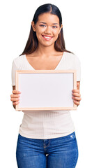 Canvas Print - Young beautiful latin girl holding empty white chalkboard looking positive and happy standing and smiling with a confident smile showing teeth