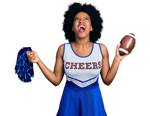 Poster - Young african american woman wearing cheerleader uniform holding pompom and football ball angry and mad screaming frustrated and furious, shouting with anger looking up.