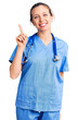 © Krakenimages.com - Young beautiful blonde woman wearing doctor uniform and stethoscope showing and pointing up with finger number one while smiling confident and happy.